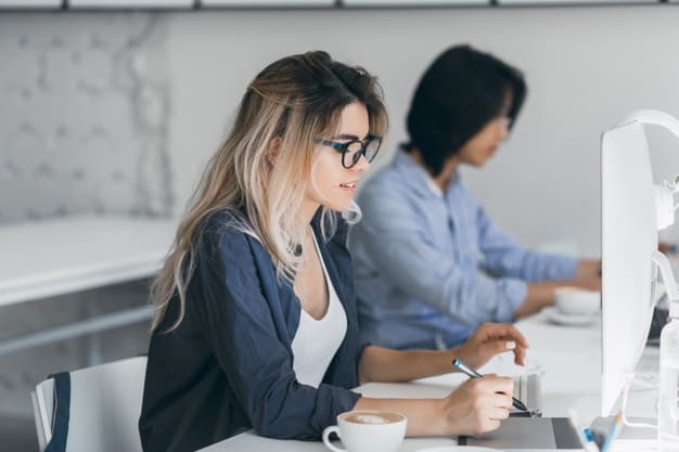 Expectativas da reforma tributária. Mulher trabalhando em frente ao computador enquanto segura uma caneta.
